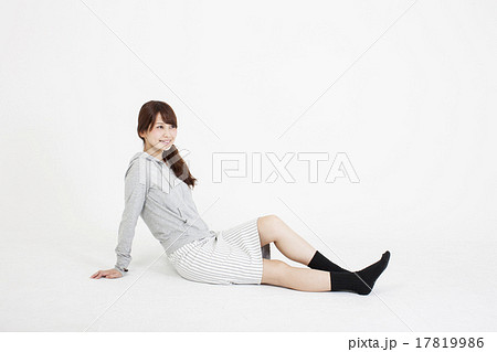 白い背景の床に足を投げ出してリラックスして座っている笑顔の若い女性の写真素材
