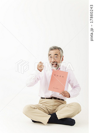 胡坐をかき年金手帳を持ちガッツポーズのシニア男性の写真素材