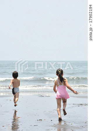 裸足で海へ駆け寄る男の子と女の子の写真素材