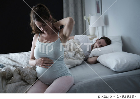 Woman sitting on bed and stretching stiff neck Woman sitting on bed and stretching stiff neck 17929387