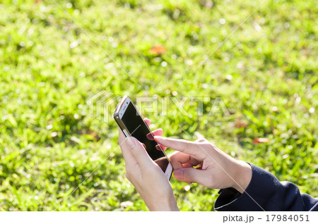 鮮やかな芝生の上でタスマートフォンを操作するビジネスマン 顔なし 鮮やかな芝生の上でタスマートフォンを操作するビジネスマン 顔なし 17984051