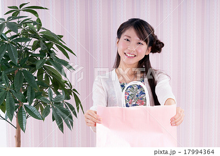 部屋でピンク色の袋に入れたプレゼントを渡す女性の写真素材