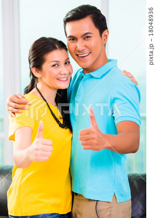 Young Asian couple in apartment with thumbs up Young Asian couple in apartment with thumbs up 18048936