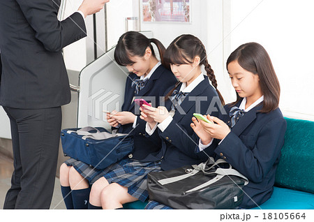 電車の中でスマホを操作する中学生の女の子の写真素材
