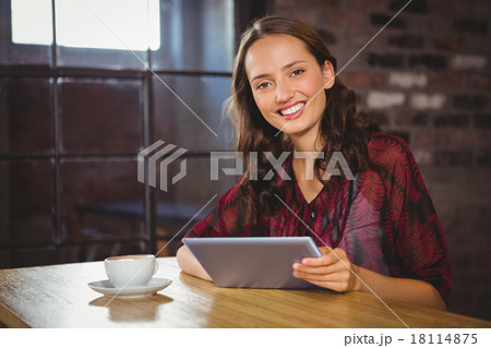 Smiling brunette having coffee and holding tablet 18114875