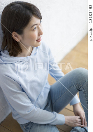 壁にもたれて座る若者女性の写真素材