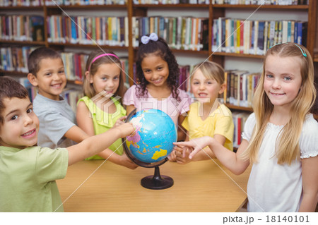 Pupils smiling at camera in library pointing to globe 18140101