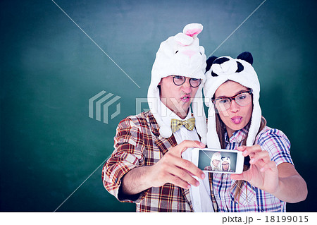 Composite image of geeky hipster couple taking selfie with smart Composite image of geeky hipster couple taking selfie with smart 18199015