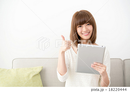 ソファに座ってタブレットを操作するミディアムヘアの若い女性 18220444