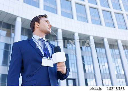 Journalist with microphone stands near the office 18243588