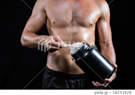 Shirtless man scooping up protein powder Shirtless man scooping up protein powder 18251626