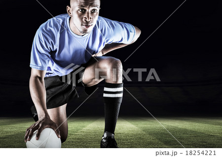 Composite image of serious rugby player kneeling while holding b 18254221