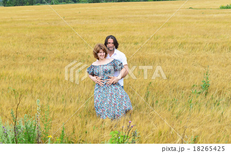 Loving middle-aged couple standing in field in summer Loving middle-aged couple standing in field in summer 18265425