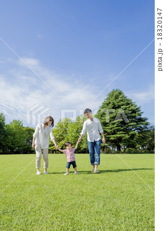 公園を手をつないで歩く3人家族 18320147