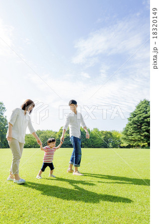 公園を手をつないで歩く3人家族 18320149
