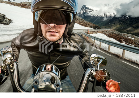 Biker in helmet and leather jacket racing on mountain serpentine 18372011