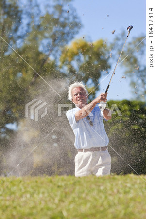 Senior man playing golf shot in a sand bunker 18412814