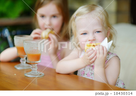 Two sisters drinking juice and eating pastries Two sisters drinking juice and eating pastries 18430314