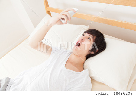 スマホを見て驚く寝起きの男性 18436205