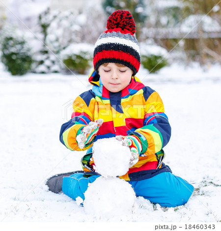 Funny preschool boy in colorful clothes making a snowman Funny preschool boy in colorful clothes making a snowman 18460343