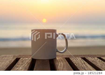 Coffee cup on wood table at sunset or sunrise beach Coffee cup on wood table at sunset or sunrise beach 18521284