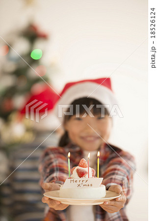 クリスマスツリーの前でケーキを差し出す女の子の写真素材