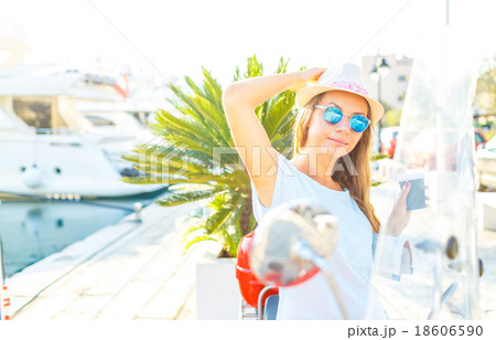 Trendy woman drinking takeaway coffee near her red moped on the Trendy woman drinking takeaway coffee near her red moped on the 18606590