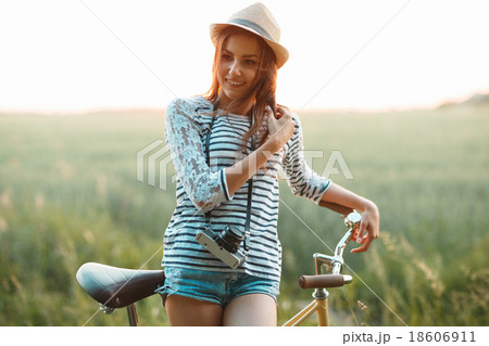 Lovely young woman stands in a field with her bicycle 18606911