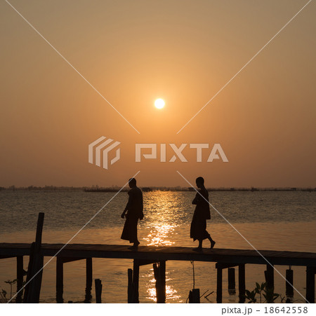 Monks crossing the bridge at sunset on lake 18642558