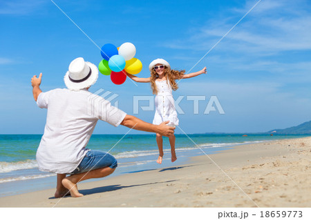 Father and daughter with balloons playing on the beach at the da 18659773