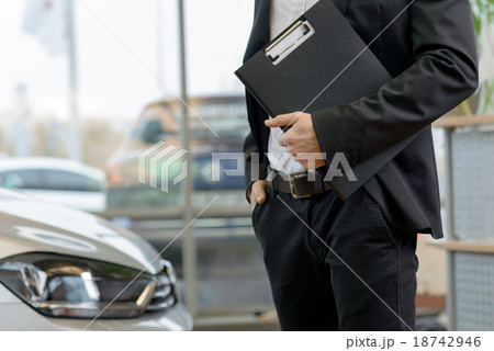 Salesman with clipboard is standing beside the car Salesman with clipboard is standing beside the car 18742946