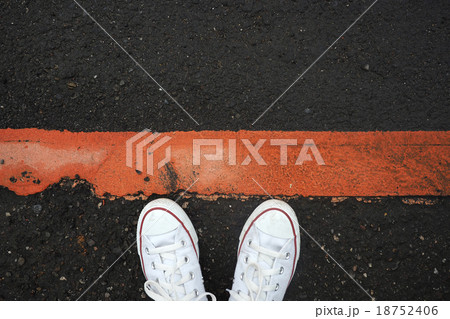 White sneaker shoes standing behind the red line. 18752406