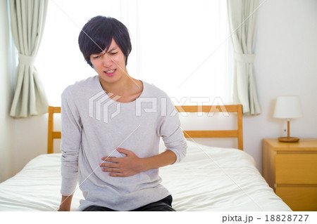 胃痛　腹痛　胃もたれ　胃腸炎　疲れ　疲労　体調不良　10代か20代の若い男性　ポートレート　部屋着 18828727