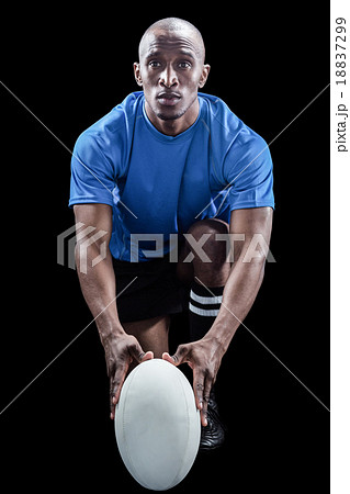 Portrait of rugby player holding ball while kneeling 18837299