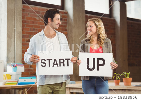 Smiling business people showing card with start up text in offic 18838956