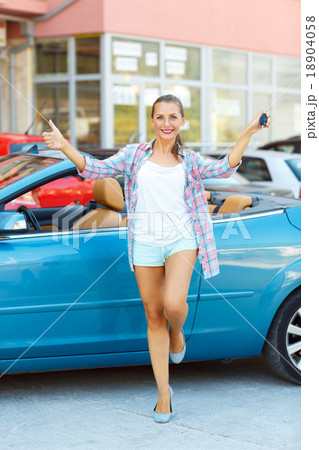 Young happy woman standing near a convertible with the keys in h 18904058