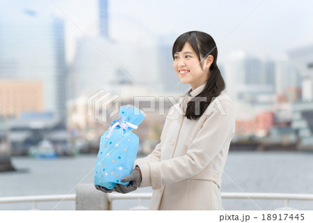 海の見える公園にプレゼントを持ってコートを着て立っている若い女性 18917445