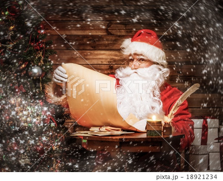 Santa Claus in wooden home interior reading wish list scroll Santa Claus in wooden home interior reading wish list scroll 18921234