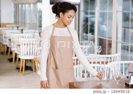 Waitress is putting water glasses on the tables. Waitress is putting water glasses on the tables. 18949618