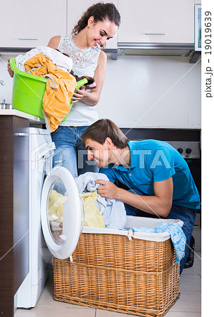 Husband helping housewife to use washing machine indoors 19019639