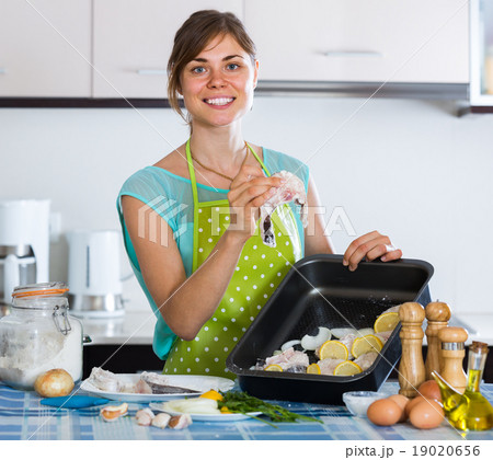 housewife putting pieces of white fish in tray 19020656