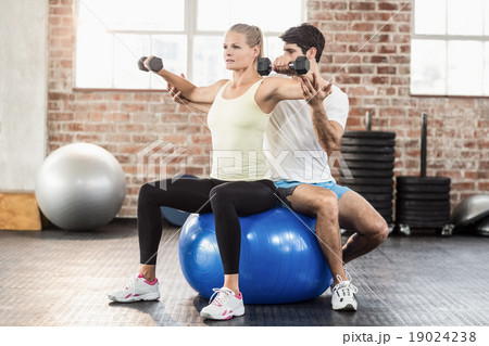 Male trainer helping young woman with the dumbbells 19024238