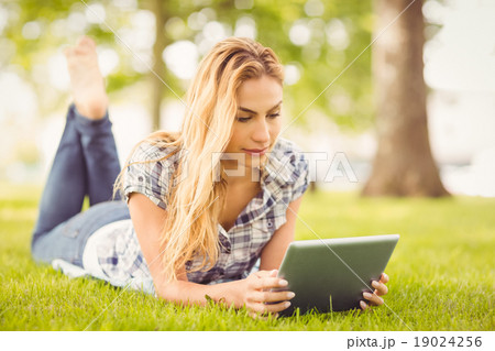 Woman using digital tablet while lying on grass Woman using digital tablet while lying on grass 19024256