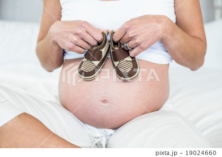 Midsection of woman with baby shoes on belly Midsection of woman with baby shoes on belly 19024660
