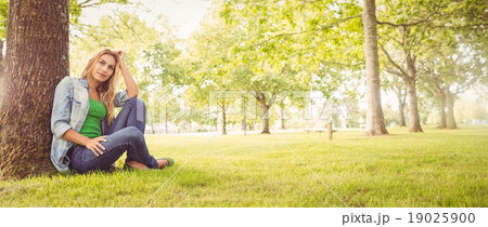 Full length of smiling woman with hand in hair while sitting und 19025900