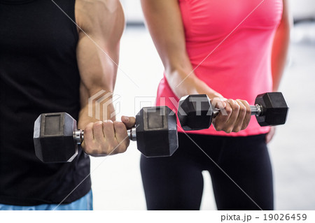 Sporty couple exercising with dumbbells i Sporty couple exercising with dumbbells i 19026459