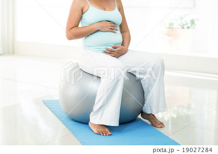 Pregnant woman sitting on exercise ball touching her belly Pregnant woman sitting on exercise ball touching her belly 19027284