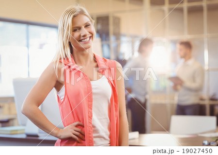 Businesswoman with hand on hip standing against male colleagues Businesswoman with hand on hip standing against male colleagues 19027450