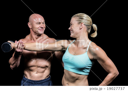 Cheerful trainer helping woman for lifting dumbbell Cheerful trainer helping woman for lifting dumbbell 19027737