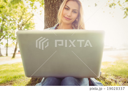 Smiling woman using laptop while sitting under tree Smiling woman using laptop while sitting under tree 19028337